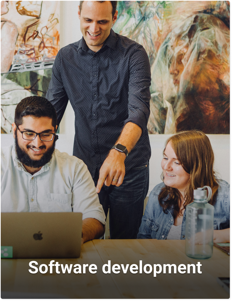 Lachende man achter laptop met collega's die naar zijn scherm kijken